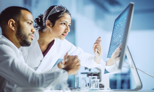 Two lab technicians collaborate while reviewing results on a computer.